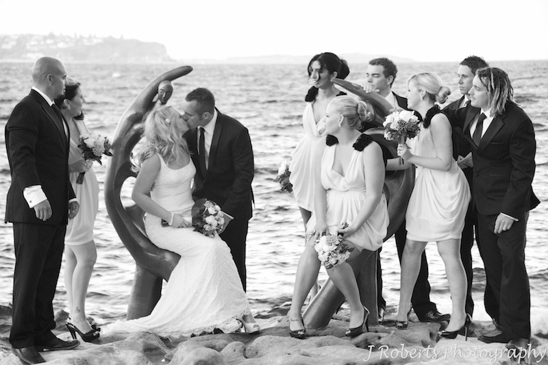 B&W of bridal couple kissing with bridal party looking on - wedding photography sydney